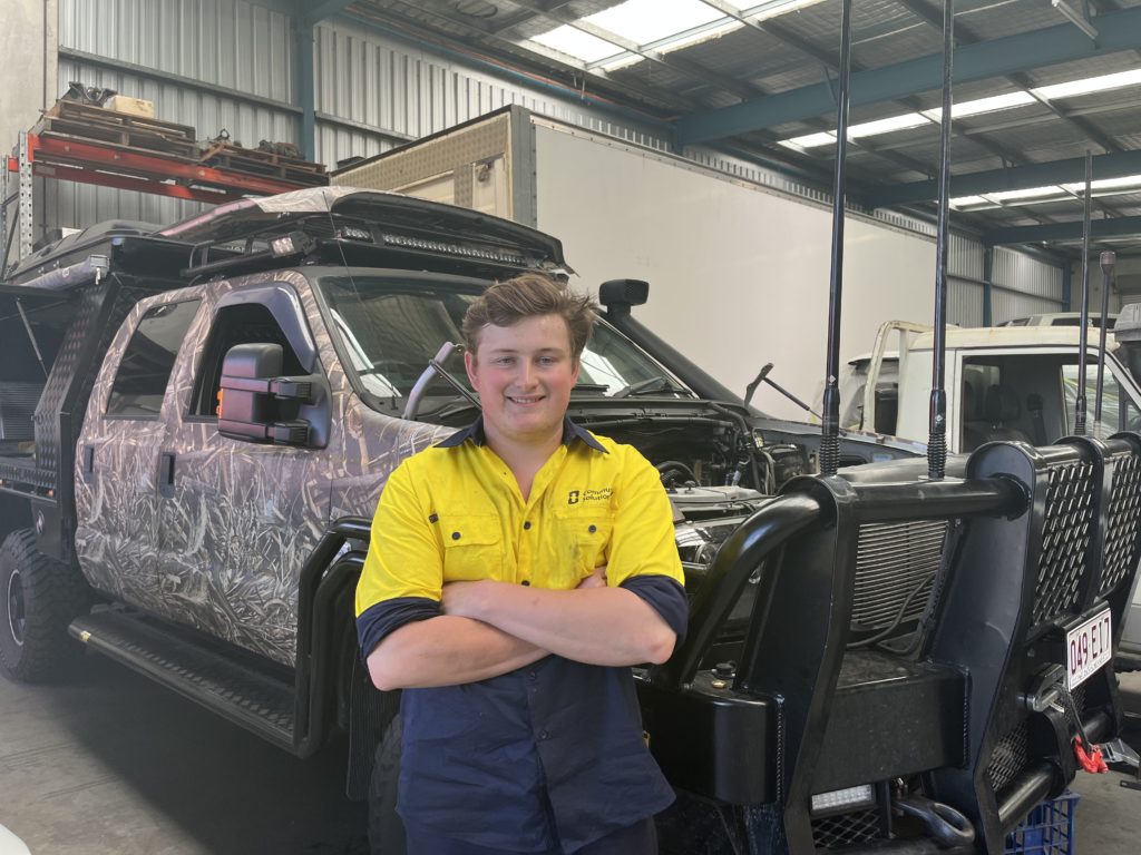 Jared stands proudly in the workshop where he is completing automotive apprenticeship